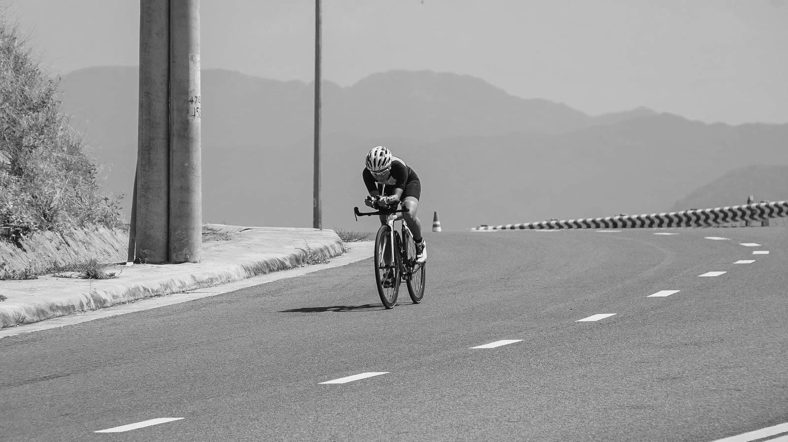 Cycliste seul en position aérodynamique sur une route dégagée, montagnes en arrière-plan